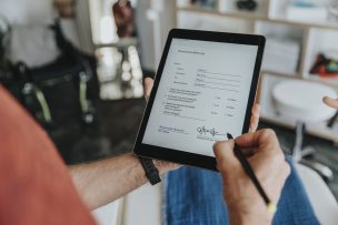 Mann schaut auf ein Tablet und unterschreibt ein Dokument