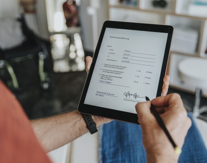 Mann schaut auf ein Tablet und unterschreibt ein Dokument